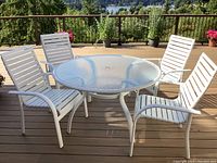 Patio table with patterned glass top and four white metal frame chairs around it.