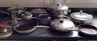 Overview of all pots and pans displayed on counter showing mix of stainless steel and non-stick cookware with glass lids and metal handles