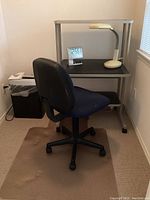 Wide view showing desk, lamp, Brookstone clock on desk, blue office chair on plastic floor mat, and Fellowes shredder at left corner