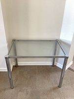 Front angled view of the small rectangular table showing clear glass top and chrome legs and side frame.