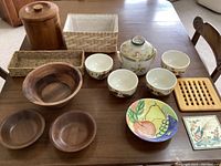 Photo of Keraluc Quimper stoneware crock, Royal Norfolk ceramic bowls, wooden bowls, woven baskets, teak ice bucket, wooden trivet, and colorful ceramic plate displayed on table.