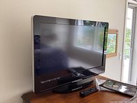 Front angle view of the Vizio 32 inch LCD HDTV flat screen TV on its stand with remote beside it on a surface.