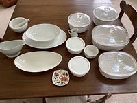Photo of complete set of white ceramic and glass dinnerware including mortar and pestle, gravy boat, serving platters, small pitcher, small floral plate, and baking dishes with glass lids.