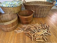 Photo of three wooden laundry baskets, a large woven wicker basket, and scattered wooden clothes pins on a wooden floor.