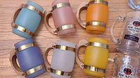 Six frosted Siestaware mugs in blue, mauve, orange, purple, white, and yellow with gold trim and handles.