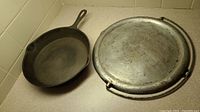 Cast iron frying pan next to metal griddle showing overall size and condition.