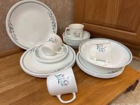 Photo showing stacked Corelle Rosemarie dinner plates, luncheon plates, bowls, small plates, and coffee mugs on a wooden surface