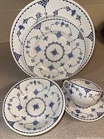Five English Ironstone place setting pieces displayed: three plates of varying sizes, a teacup, and a saucer. Blue floral and vine patterns on white ironstone.