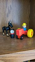 Vintage Fisher Price farm figures including tractor, farmer, black horse, and dog missing an ear on wooden surface