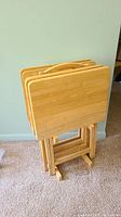 Four small folding wooden tray tables stacked in the wooden caddy, shown from front angle.