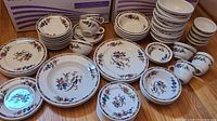 Wide view showing cups, saucers, plates, bowls arranged on floor with floral and bird motifs in multicolor Syracuse China pieces.