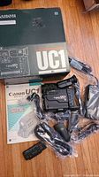 Canon UC1 camcorder with original box, manual, remote, cables and accessories laid out on wooden floor