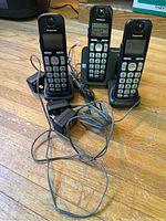 Full view of the Panasonic telephone system showing three cordless handsets placed on their charging docks with power adapters and cables visible.