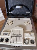 Close-up of the reel to reel tape recorder unit showing front panel buttons, dials, input/output jacks, and branded stop/play/speaker/record controls.