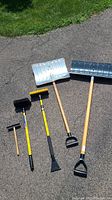 Full view of all snow shovels, brushes and scrapers on pavement showing condition and size.