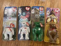 Four Ty Beanie Babies packaged, including Maple, Glory, Erin, and Britannia bears.