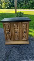 Front view of ornate vintage bar/side table showing carved two-door panels and metal handles on each door.