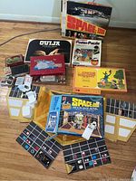 Photo of various vintage board games including Space 1999 board game, Ouija board box, Bingo game box with chips, Uncle Wiggly game, and a poster puzzle in original boxes on floor.