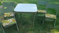 Full set of one folding card table and four folding chairs on grass outdoors.