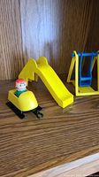 Yellow slide, playground vehicle with attached black components, and red-haired figure placed on a wooden surface