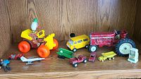 Shelf display showing colorful vintage toys including a Fisher Price Jalopy toy, metal bus, tractor, and smaller toy vehicles.