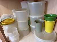 Photo showing stacked vintage translucent plastic Tupperware storage containers and three colorful tumblers in green, yellow, and gray.
