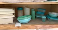 Wide shot showing assortment of vintage Tupperware items on shelf including rectangular containers, nested bowls, and assorted shaker bottles and small containers.