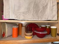 Full view of vintage Tupperware items on a kitchen shelf, showing various containers, bowls, stackable cups, and a clear food strainer.