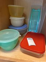 Shelf display of 7 vintage Tupperware items including various colored bowls with lids, rectangular container and grater