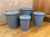 Four vintage blue Tupperware canisters of various sizes grouped on a wooden floor against wall