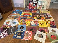 Vintage vinyl records laid out on floor showing multiple 45 RPM singles and children's LPs with varied colorful covers including albums with cartoon characters and holiday themes.