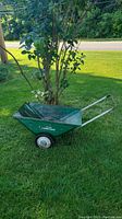Side and partial front view of the vintage green Wizard Lawn-Cart on grass, showing the full cart and wheel with white rim.