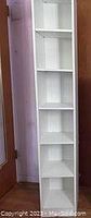 Photo of tall, narrow white laminate shelf with six evenly spaced shelves