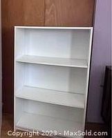Photo of a white laminate shelf unit with three shelves against a wood panel and purple wall background.