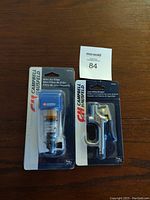 Photo showing the two Campbell Hausfeld products in original packaging on wooden surface with inventory tag nearby.