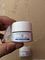 Photo of small white jar of Cellex-C Enhancer Eye Balm, held in hand, showing front label with product details