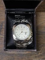 Front view of the French Connection men's wristwatch in its box, showing the white dial, stainless steel round case, and bracelet wrapped in protective plastic.