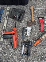 Close up of select tools such as the hand axe, air staplers, limb cutter, and part of the tool pouch.