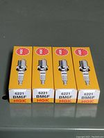 Four NGK 6221 BM6F spark plugs boxes lined up showing branding and model number.