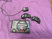 Wide view of console, two controllers and power adapter on purple surface