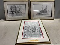 Three framed and matted black and white Clark M. Goff Boston landmark prints including a cobblestone street scene, historic building, and pond with swan boats, displayed upright on a shelf.
