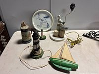 Full view of the Cape Cod decor set including wooden sailboat, seagull lamp, lighthouse, ceramic mug, and decorative platter.