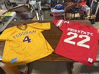 Both jerseys flat on a wooden table showing Fordham yellow jersey with maroon lettering and Ohio State red jersey with white lettering and number 22