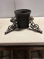 Front view of cast iron Christmas tree stand showing embossed patterns and three supporting legs with curled scrollwork.