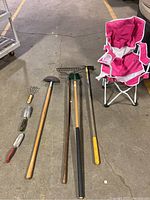 Overview of garden tools and pink folding chair on a concrete floor showing all tools and the chair in one photo
