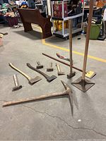 Full view of all tools laid on concrete floor including sledgehammers, axes, tamper, edger, and pickaxe