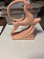 Side angle showing the lustrous pink porcelain ram with arched horn and stylized dynamic pose on sculpted base.