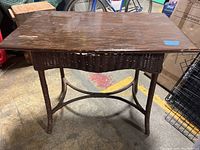 Full view of wood-topped table with brown wicker base, showing wood wear and wicker damage.