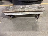 Front view of a low vintage wooden bench showing worn wood and paint splatters on planks.