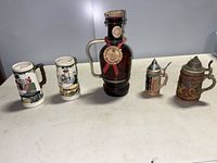 Wide view showing all 5 items including bottle, matching steins and decorative steins with pewter lids.